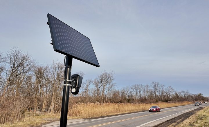 A Flock surveillance camera next to a road.