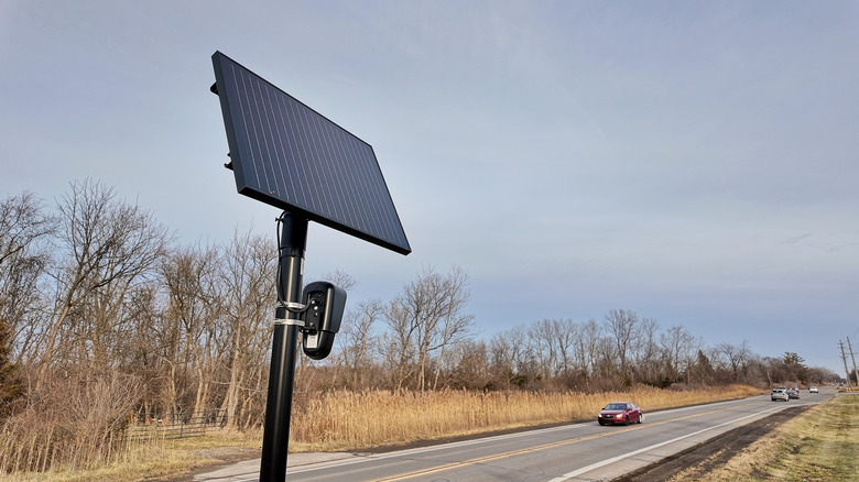A Flock surveillance camera next to a road.