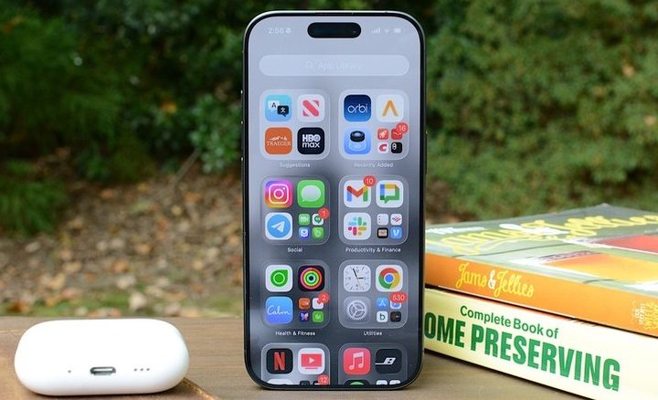 An iPhone 17 sits next to an AirPods Case and a couple of books.